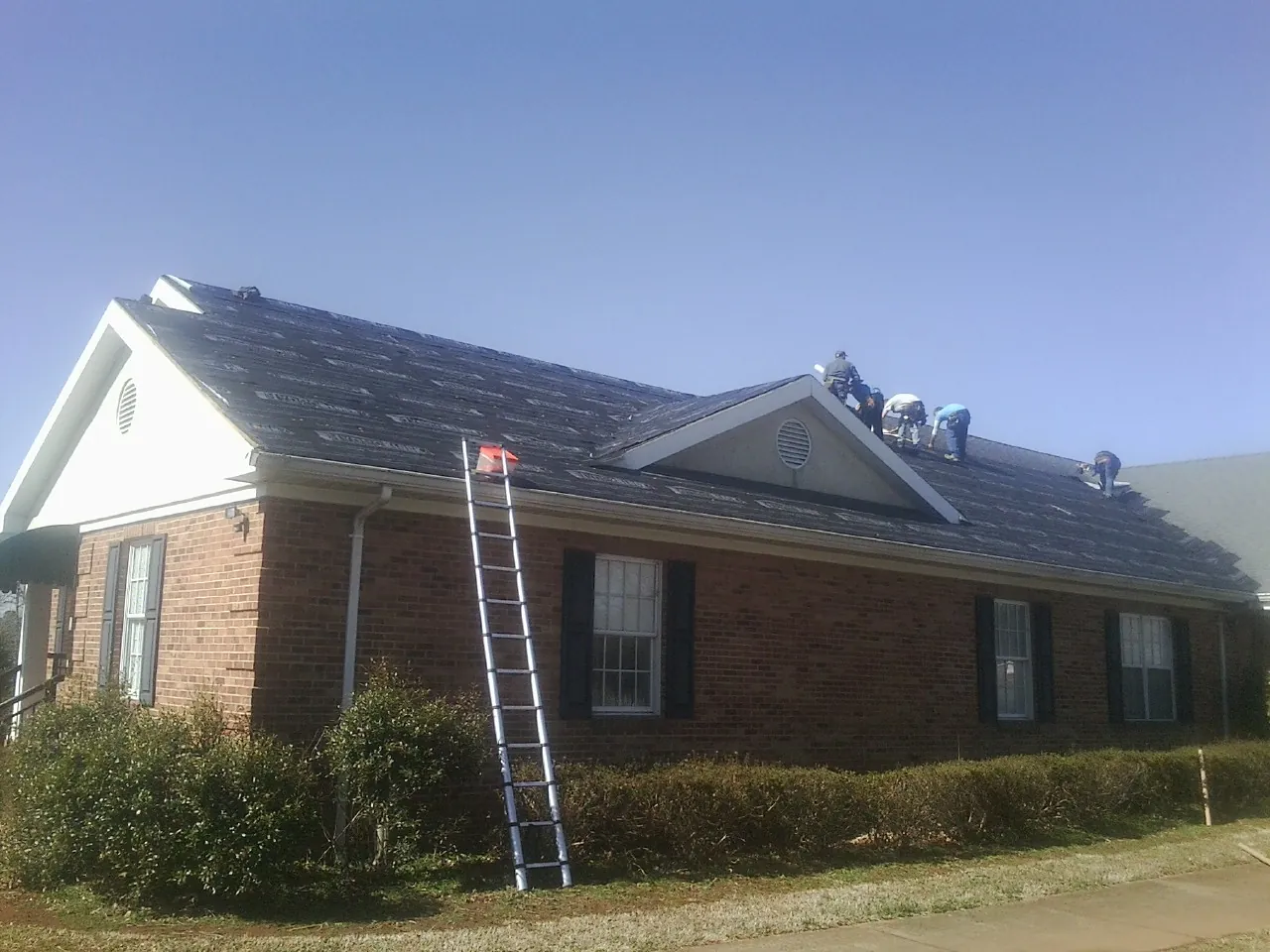 Crew tearing shingles off a brick ranch roof with a ladder set — Emergency Roof Repair work by our crew in Mount Wolf