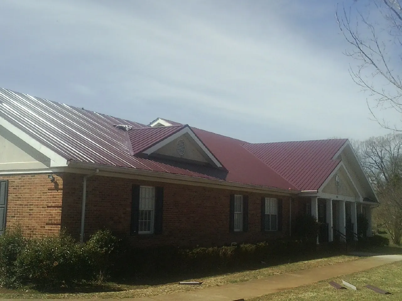 Red metal roof with gabled entries on a long brick building, from a Hail Damage Roof Repair job in Mount Wolf