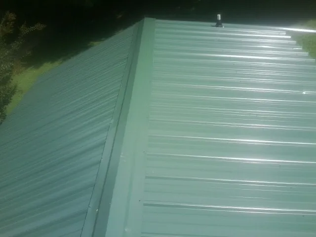 New green metal panels meeting at the ridge of a roof — Flat Roof Repair work by our crew in Mount Wolf