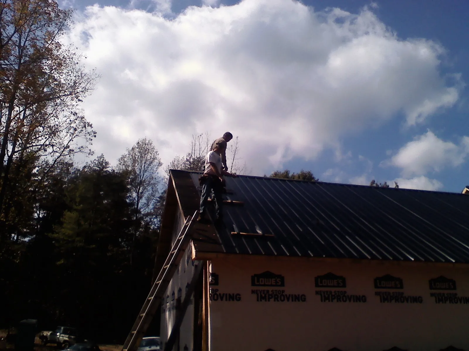 Roofer fastening dark metal panels high against a cloudy sky, from a Roof Inspection job in Mount Wolf